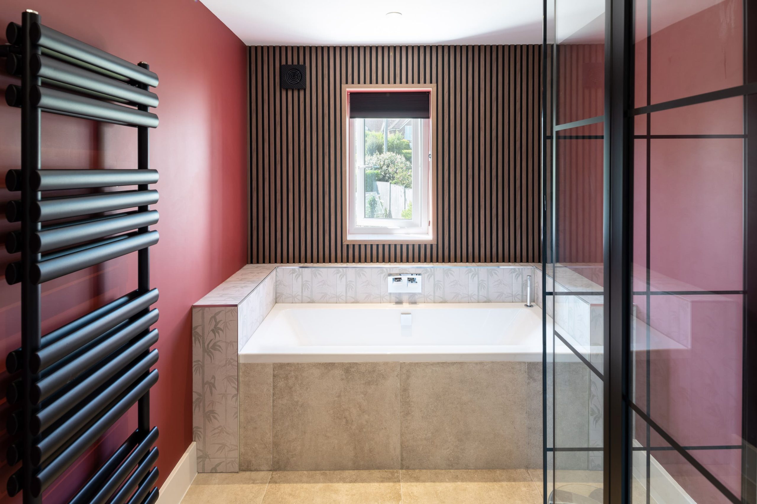 Modern bathroom with built-in bath, red feature wall, black heated towel rail and walk-in shower by PB Kitchens & Bathrooms