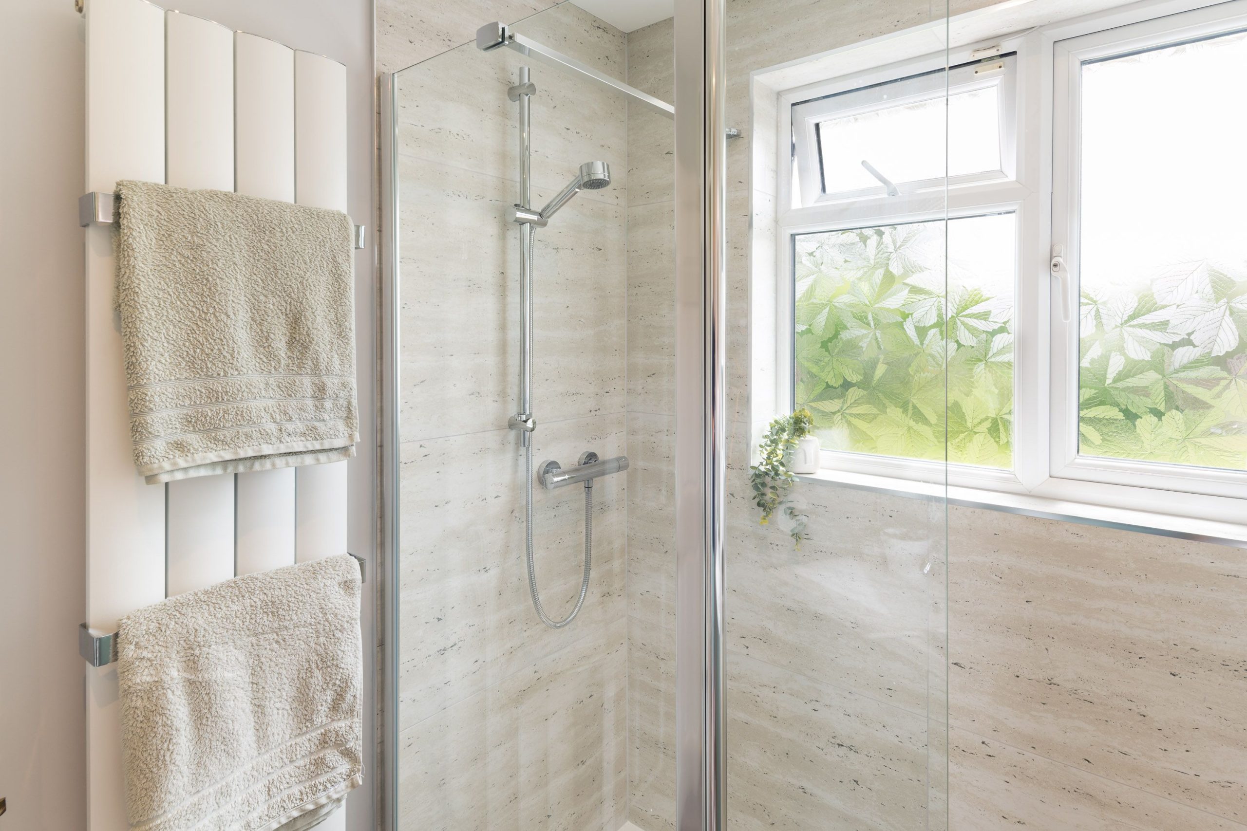 Walk-in shower with neutral stone-effect tiles, glass screen and white heated towel rail by PB Kitchens & Bathrooms