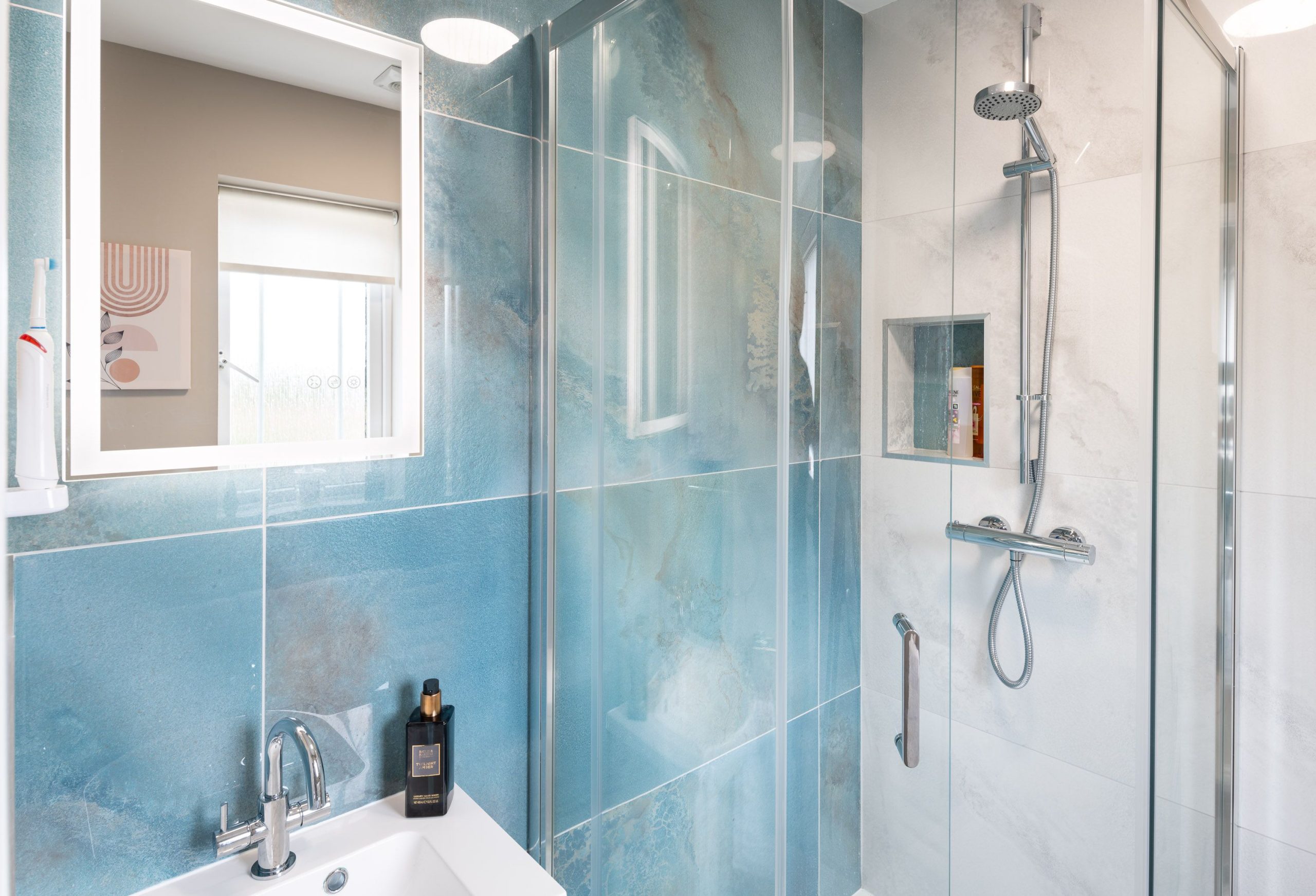 Modern bathroom with blue marble-effect tiles, glass shower enclosure and illuminated mirror