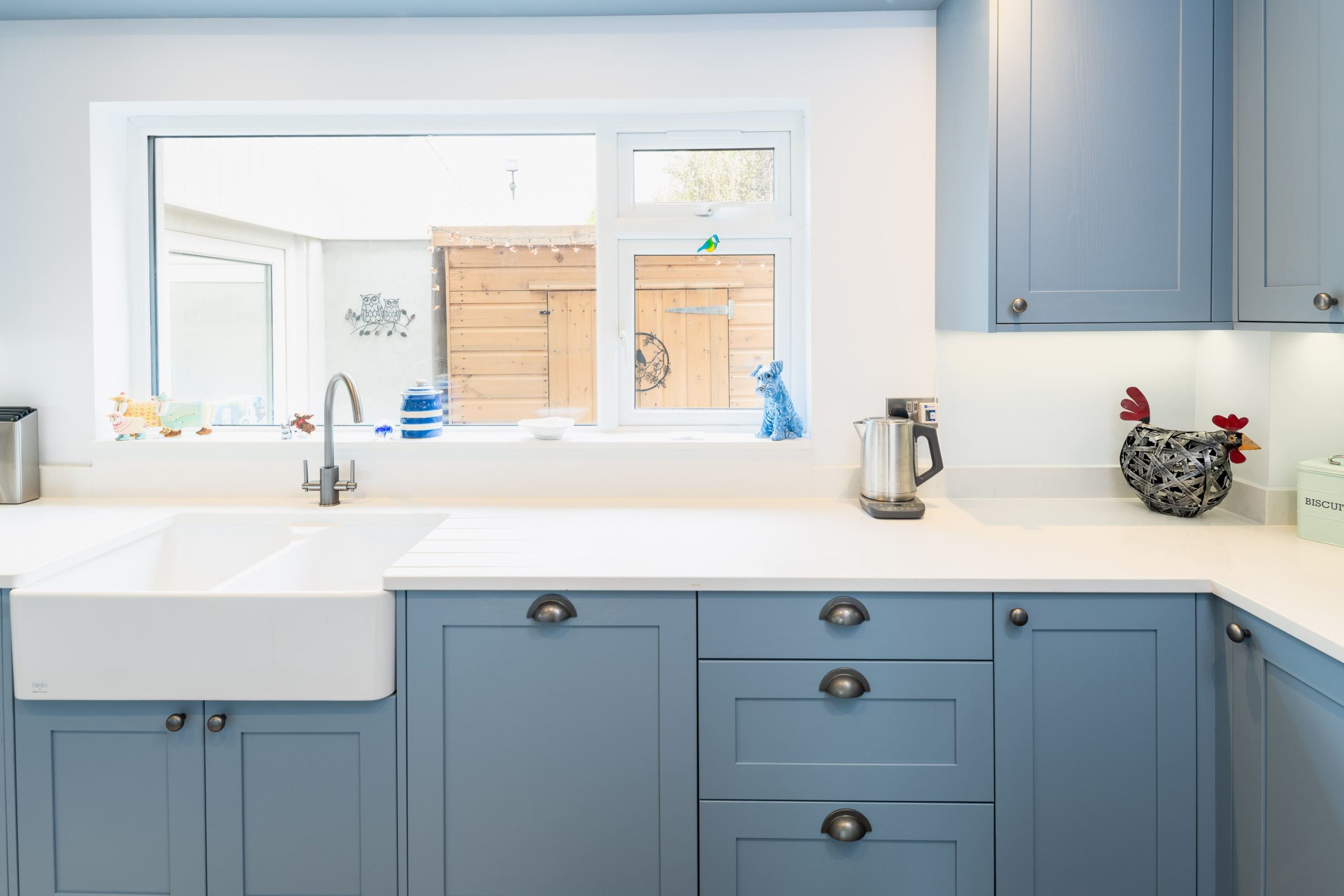 Close-up of blue shaker kitchen cabinets with white worktops, farmhouse sink and cup handles by PB Kitchens & Bathrooms