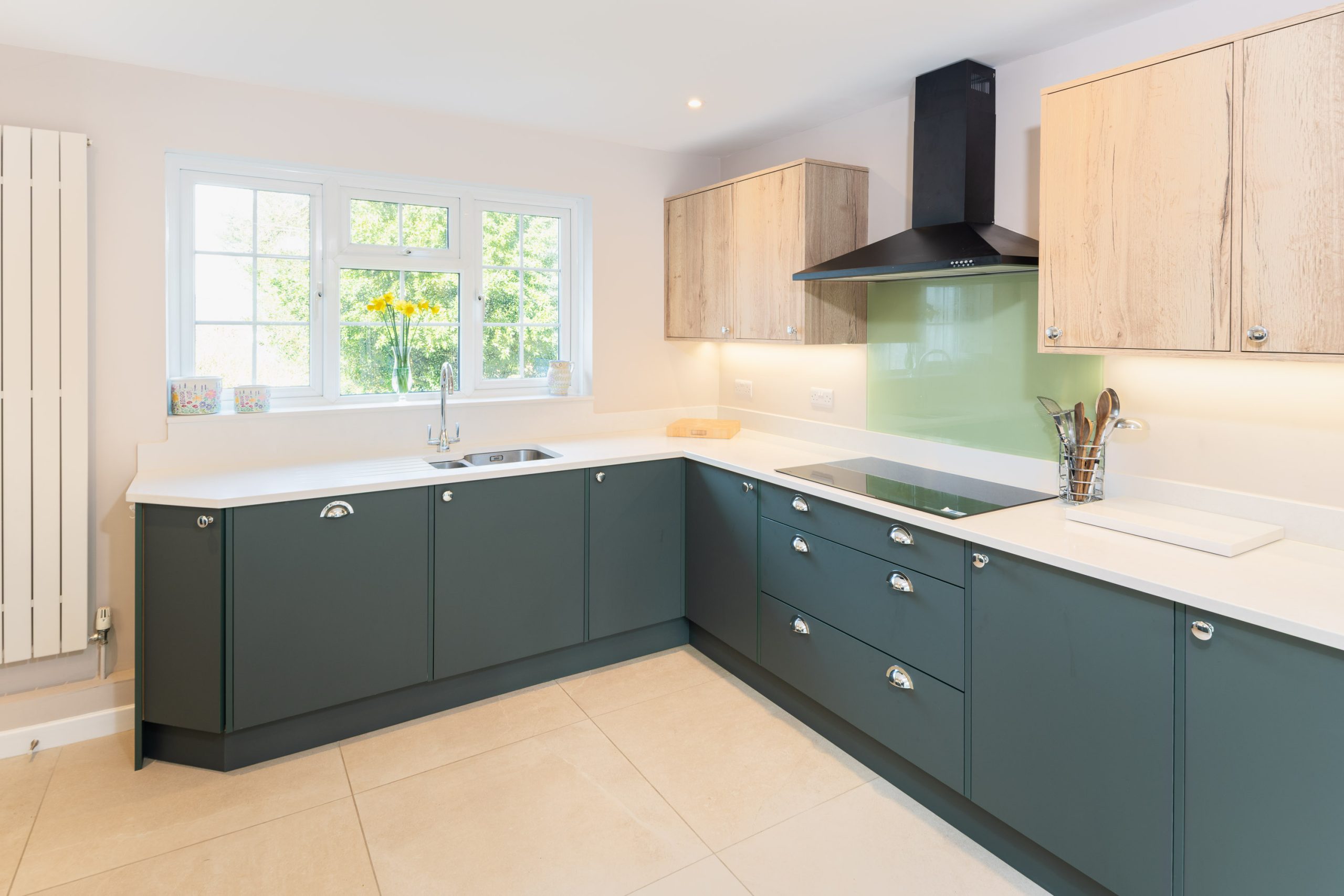 Contemporary dark green kitchen with white worktops, chrome handles and glass splashback by PB Kitchens & Bathrooms