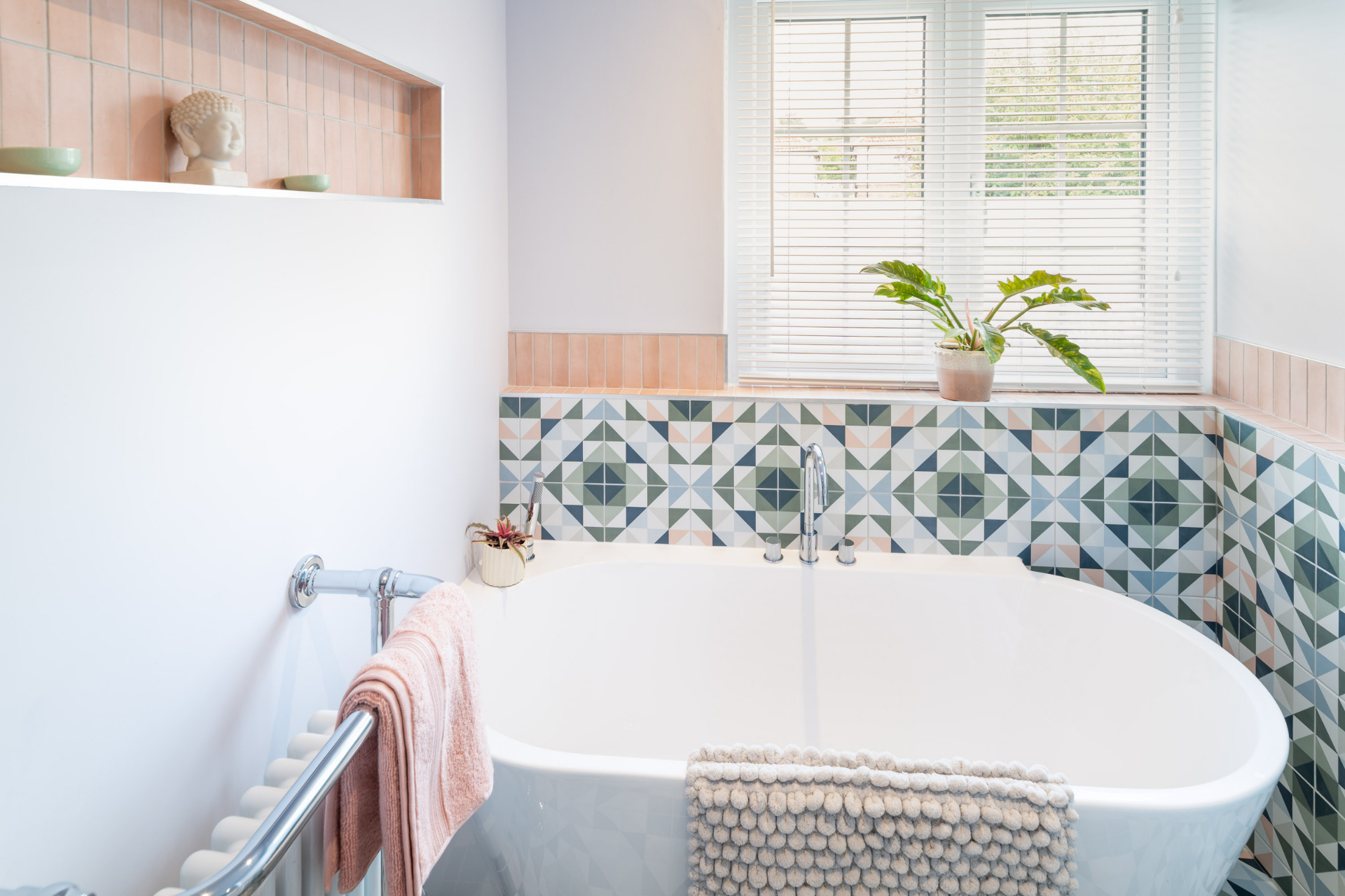 Freestanding bath with patterned wall tiles and soft pink accents in a stylish modern bathroom by PB Kitchens & Bathrooms