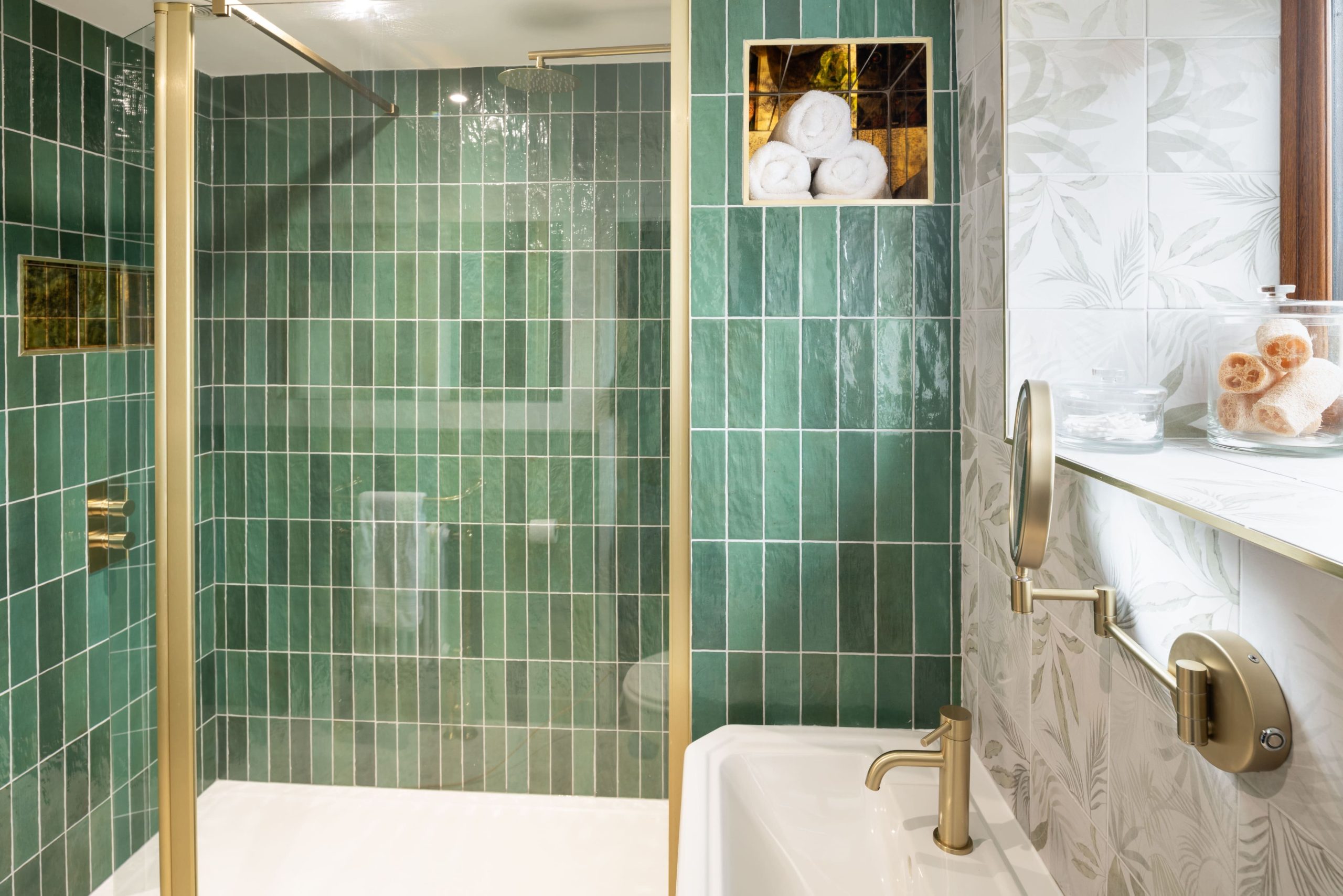 Luxury bathroom with green metro tiles, gold fixtures and fittings, glass shower screen and floral feature wall tiles